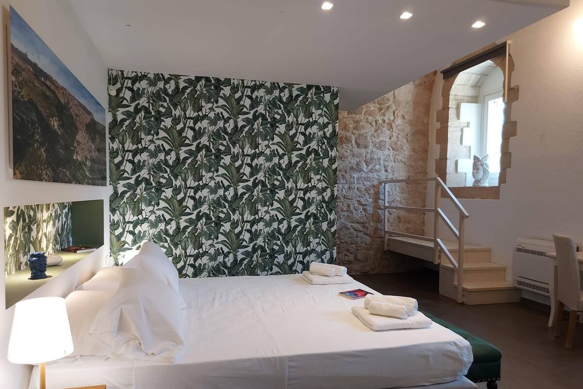 A modern hotel room with a large bed, a desk, and a staircase leading to an upper level.