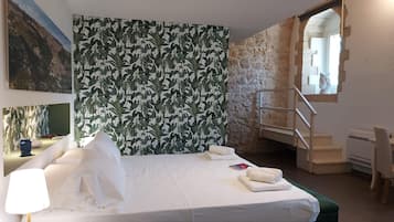 A modern hotel room with a large bed, a desk, and a staircase leading to an upper level.