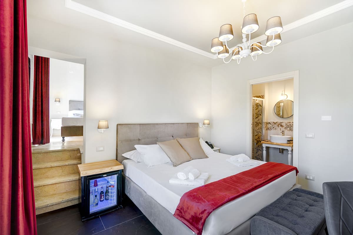 A hotel room with a bed, bedside table, refrigerator, and a mirror.