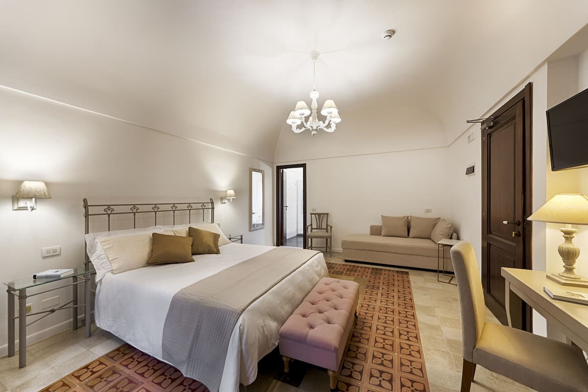 A bedroom with a bed, bedside tables, a bench, a desk, and a TV.