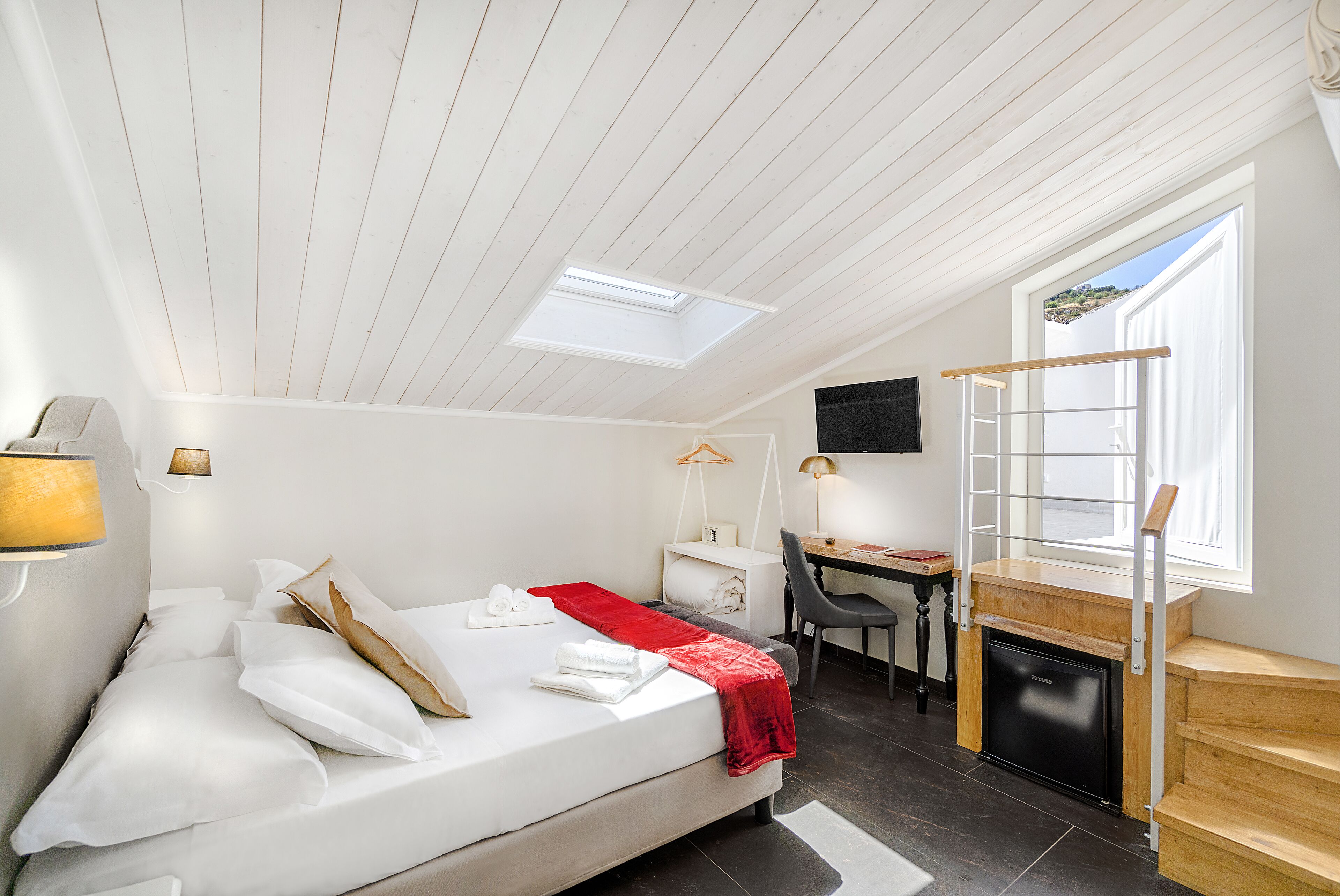 A bedroom with a bed, desk, and a TV mounted on the wall.