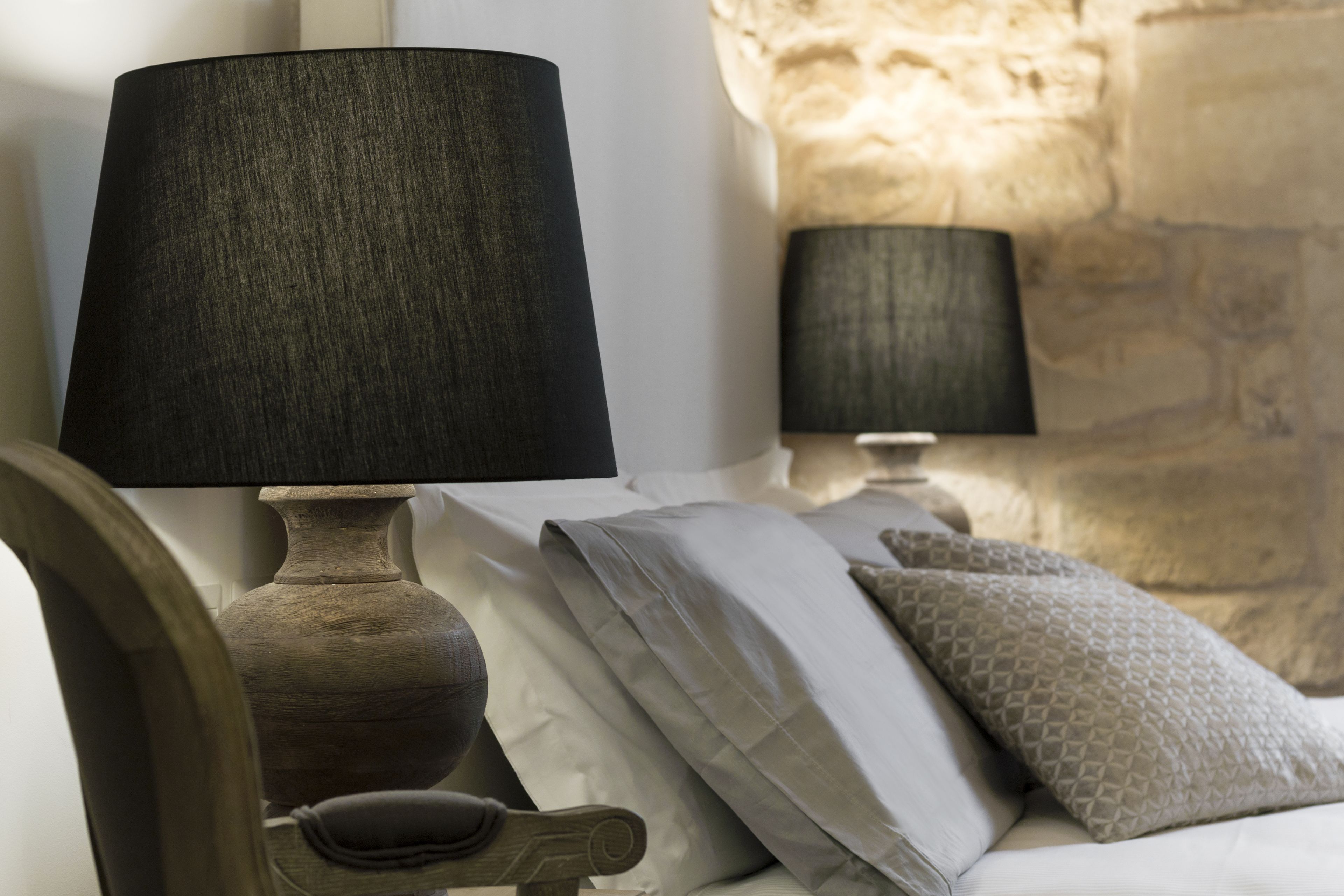 A bed with two lamps, a stone wall, and a wooden chair.