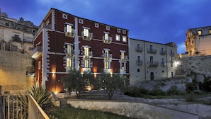 A multi-story building with balconies, a stone wall, and a grassy area in front. - Itria Palace (Ragusa)