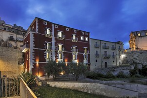Un edificio de varios pisos con balcones, un muro de piedra y una zona verde al frente.