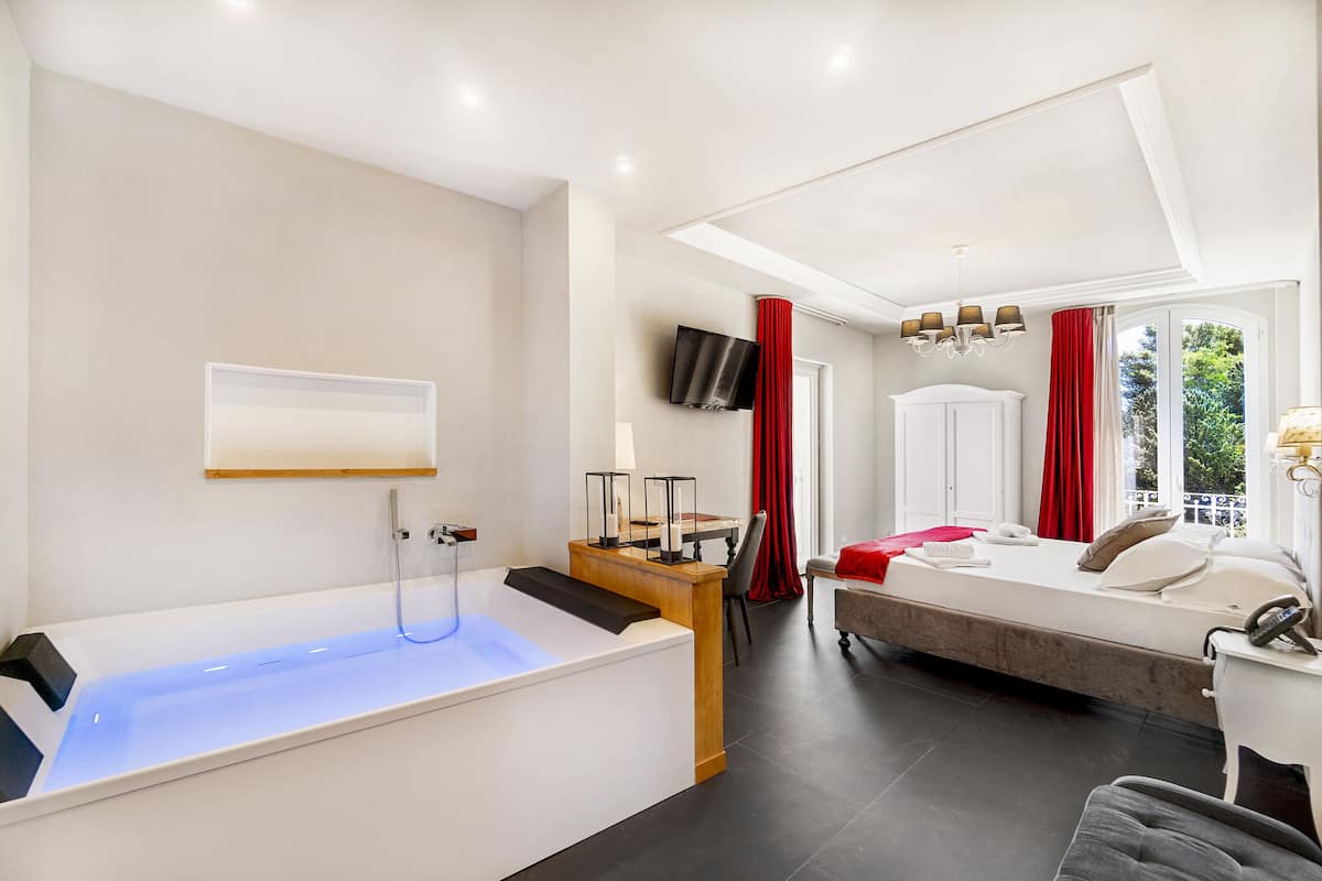 A modern hotel room with a bathtub, a bed, a desk, and a TV.