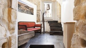 A narrow stone-walled corridor with a wooden staircase, a bench, and a framed picture on the wall. - Itria Palace (Ragusa)