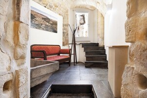 Un estrecho pasillo de paredes de piedra con una escalera de madera, un banco y un cuadro en la pared.