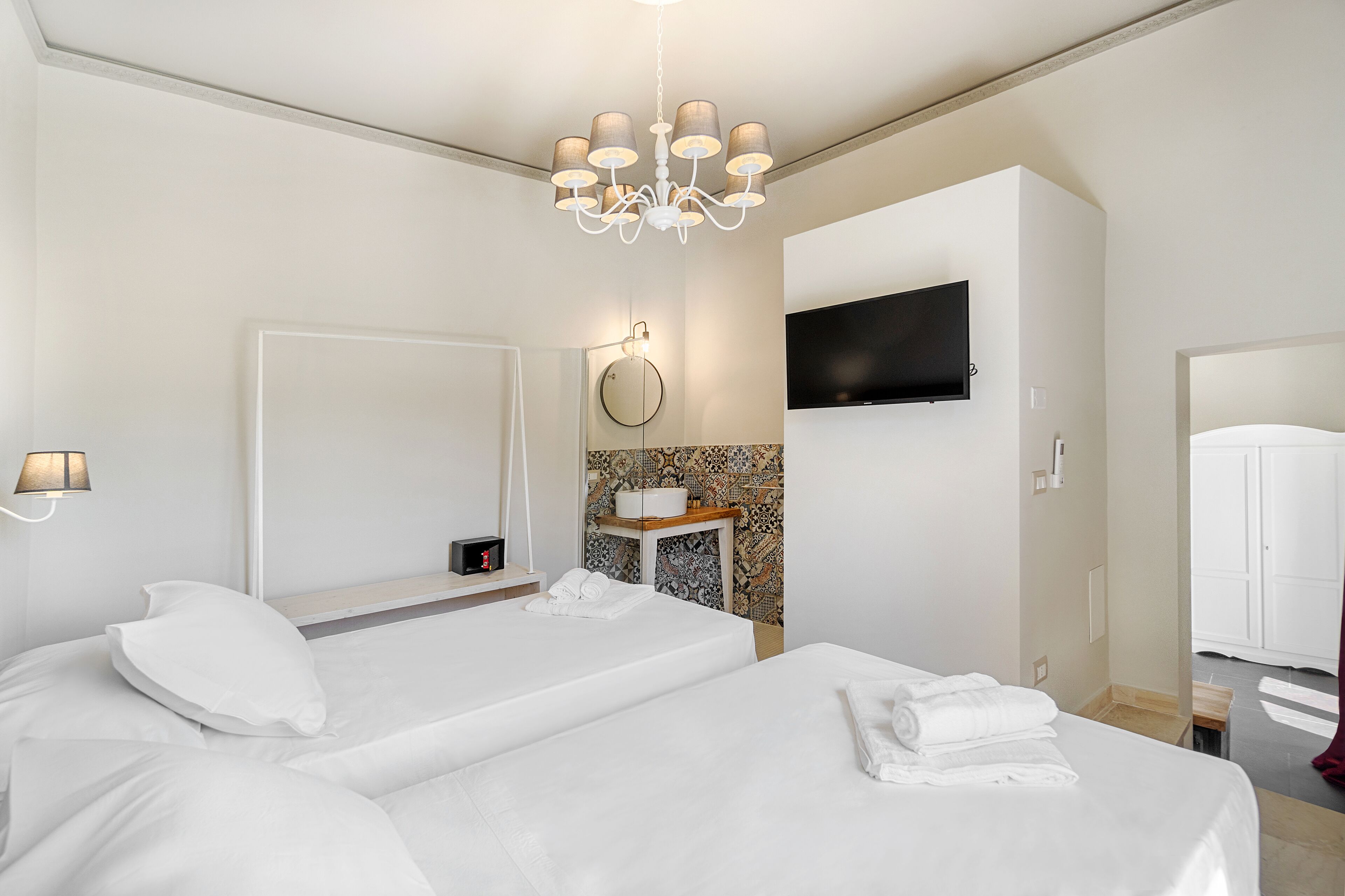 Habitación de hotel con dos camas, un televisor en la pared, un espejo y una mesita con una toalla.