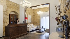 A reception area with a wooden desk, a white sofa, and a chandelier. - Itria Palace (Ragusa)