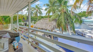 Ein Balkon mit Korbmöbeln, einem Reetdachhaus und Blick auf einen Yachthafen mit Booten.