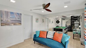 Ein Wohnzimmer mit blauem Sofa, Deckenventilatoren, einem Billardtisch und einer Treppe zu einer weiteren Ebene.
