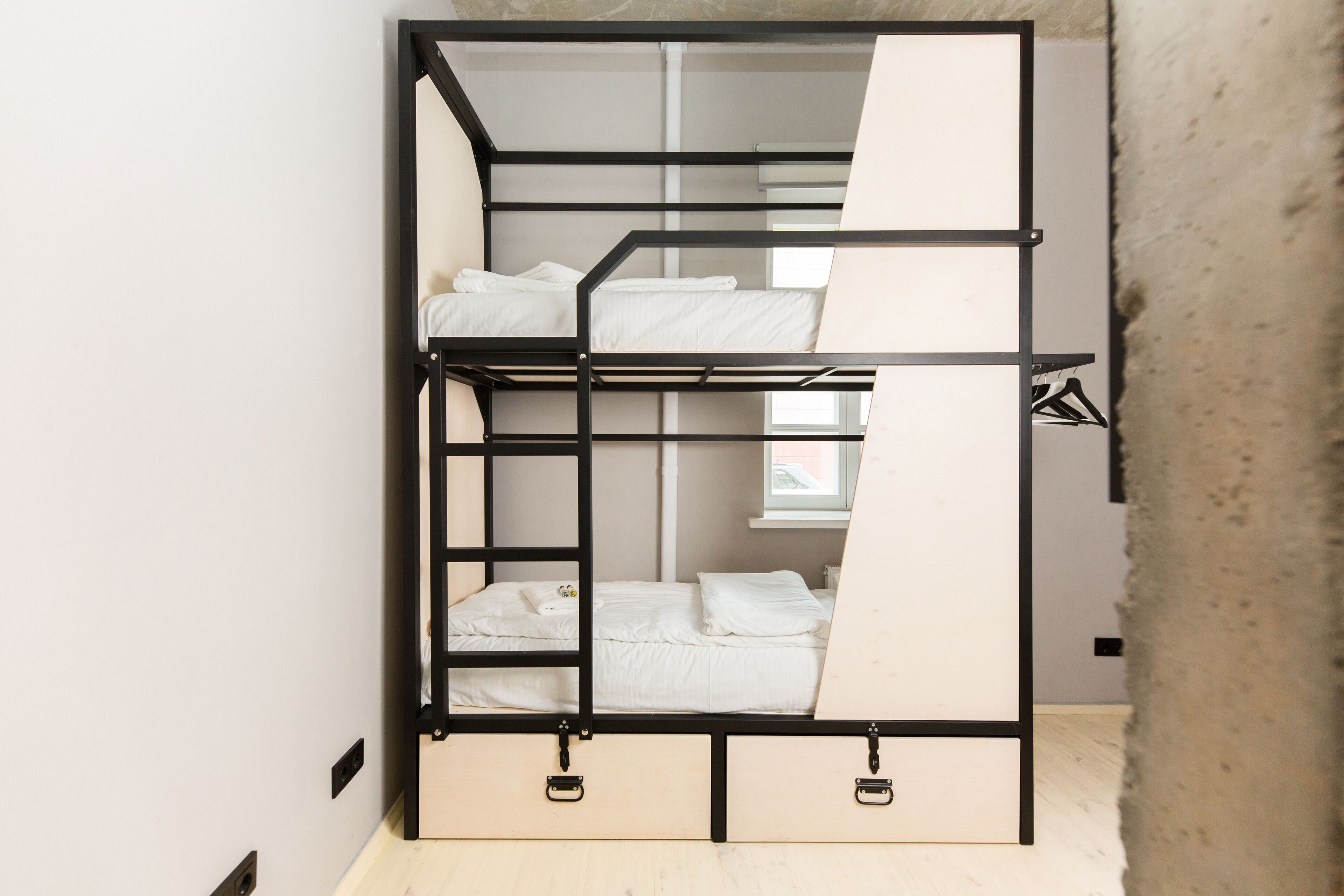 A bunk bed with a ladder, a window with a view, and a concrete wall.