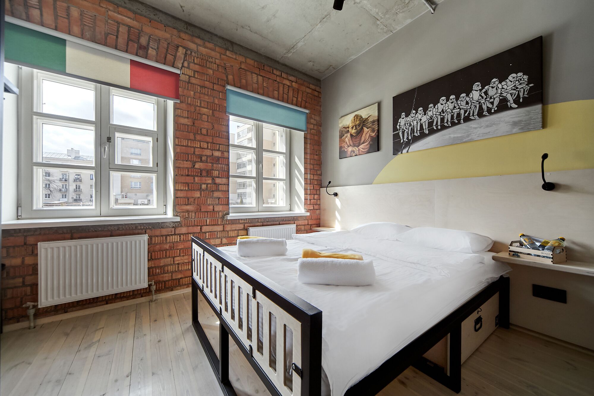 A bedroom with a brick wall, a large window, a bed with white bedding, and a nightstand with a lamp.