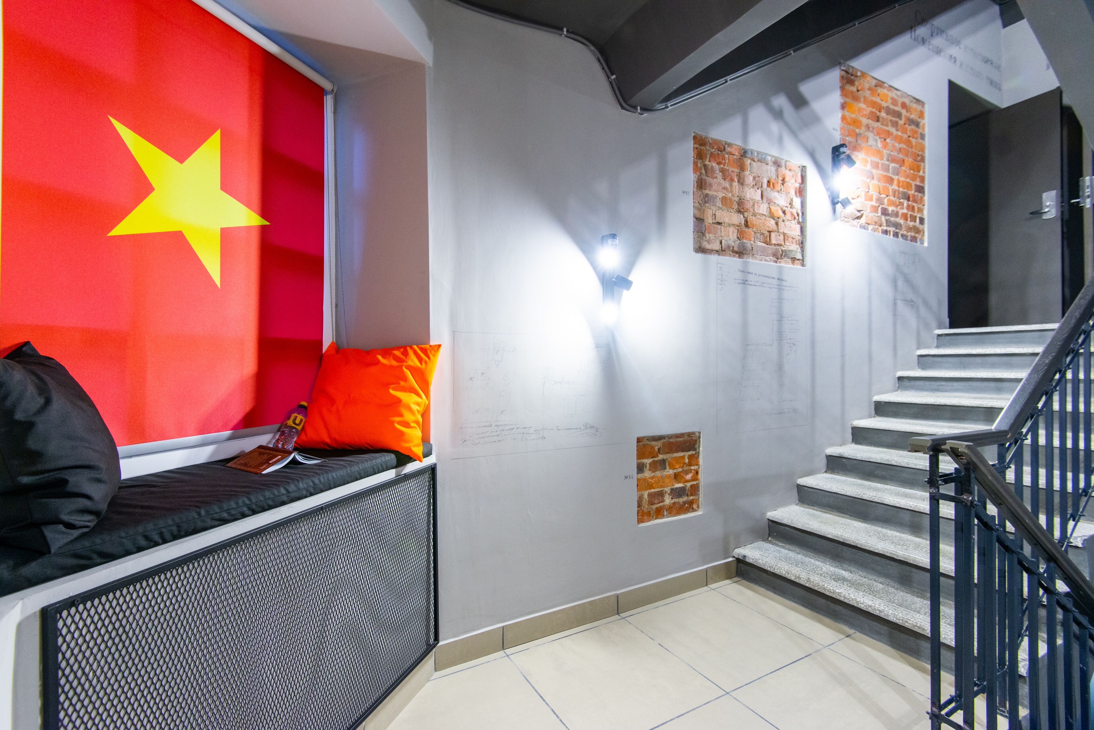 A staircase with a metal railing, a wall with a large flag, and a bench with a cushion.