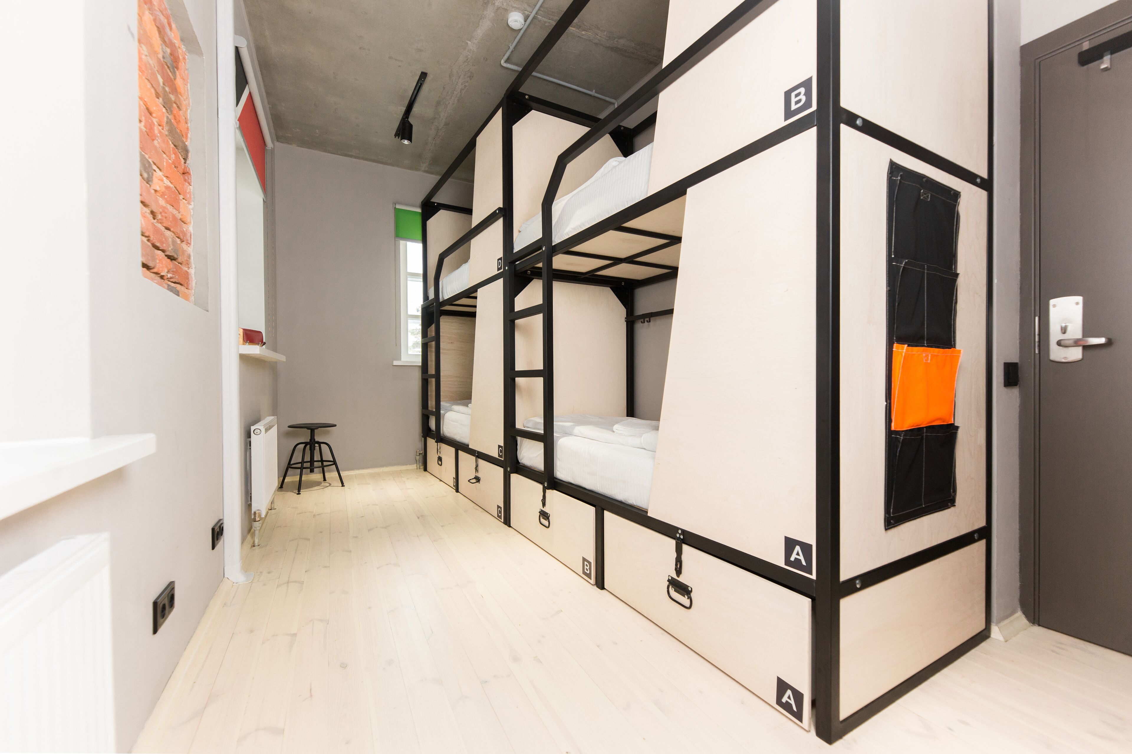 A dormitory room with bunk beds, a radiator, a small stool, and a door with a handle.