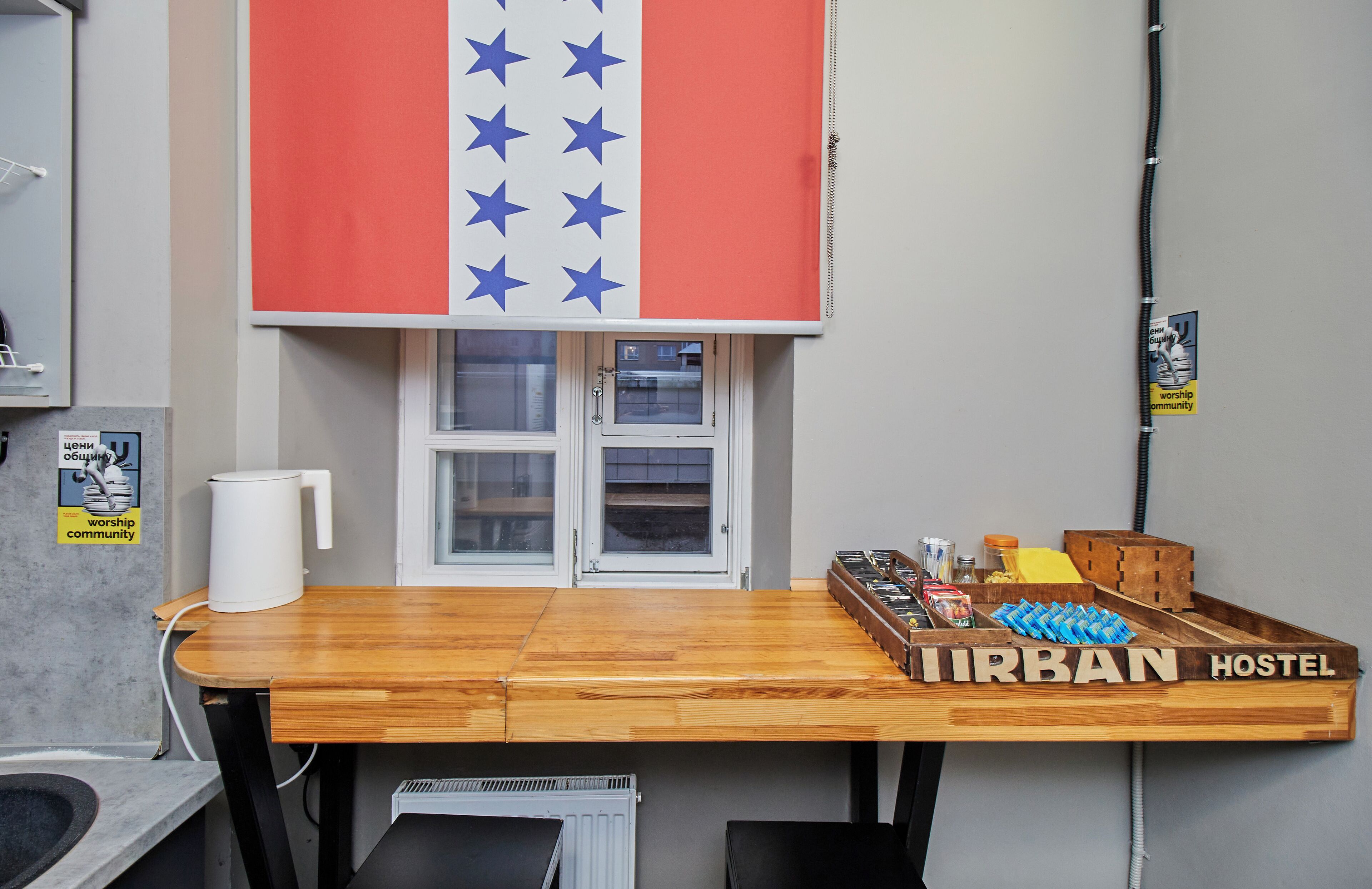 Een hostelkamer met een houten tafel, een raam met uitzicht en een bordje met de naam van het hostel.