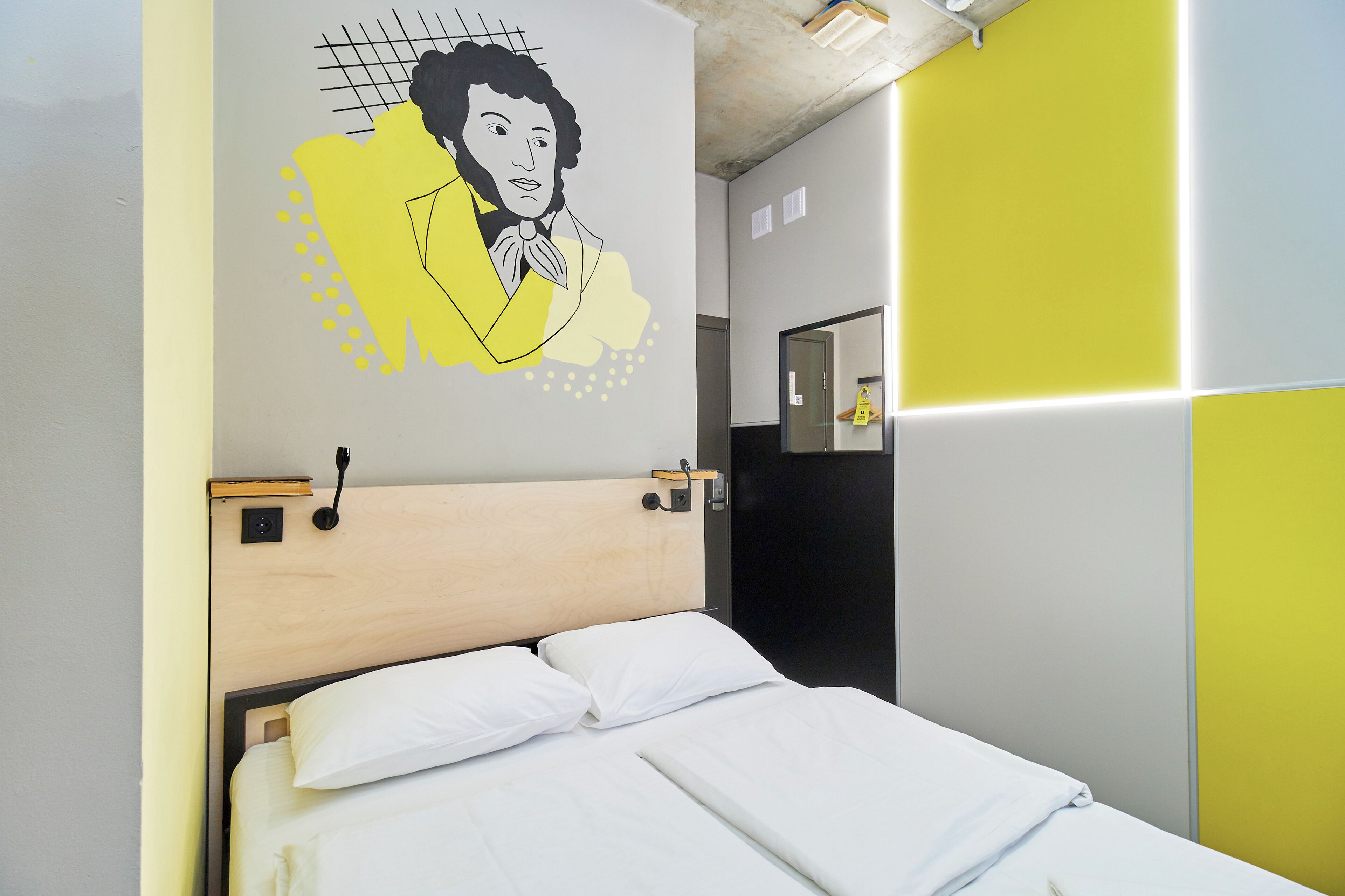 A neatly made bed with white linens, a wooden headboard, and a wall-mounted light fixture.