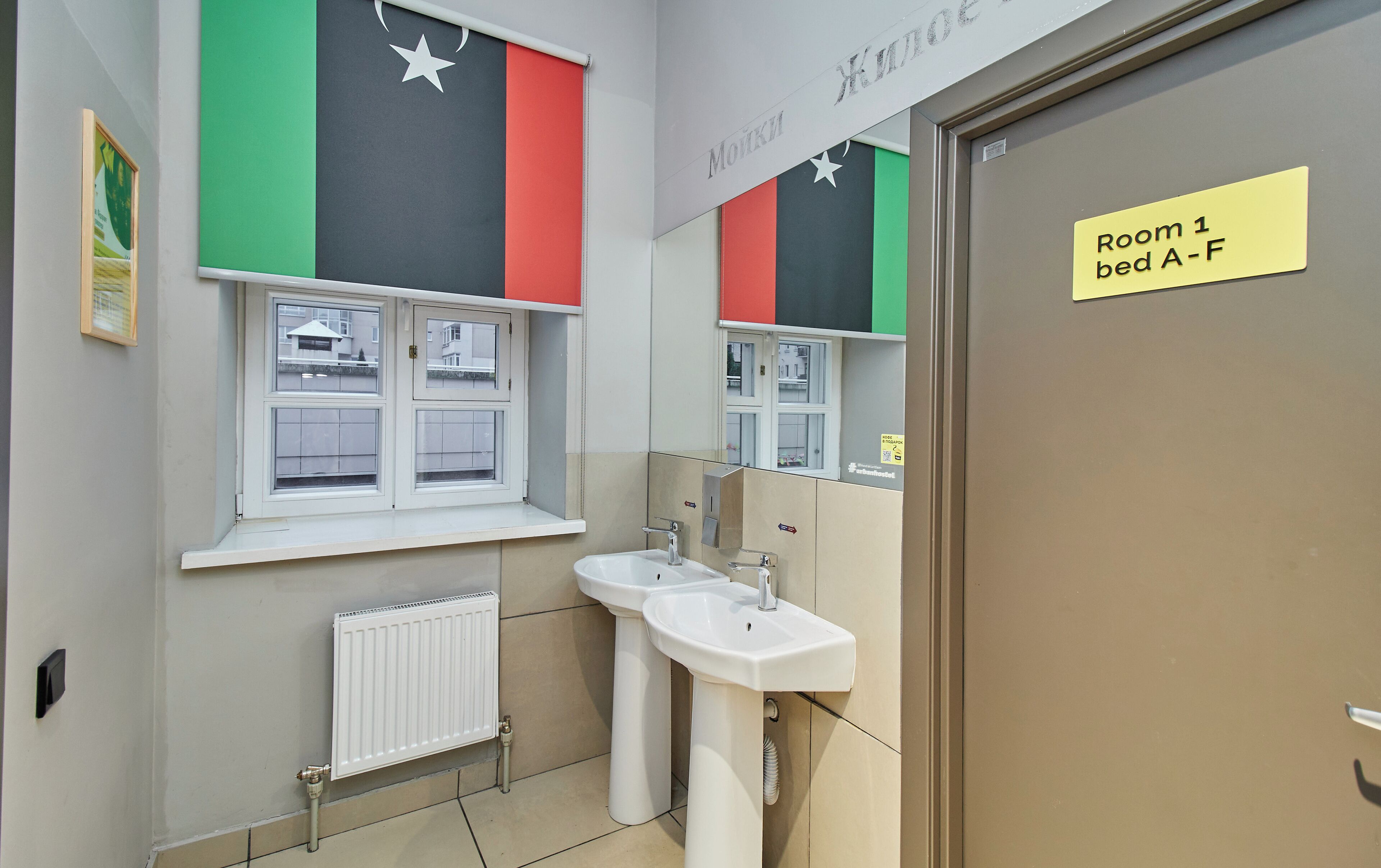 Un baño con ventana, un radiador y un lavabo. Hay un cartel que indica la habitación 1, camas A-F.