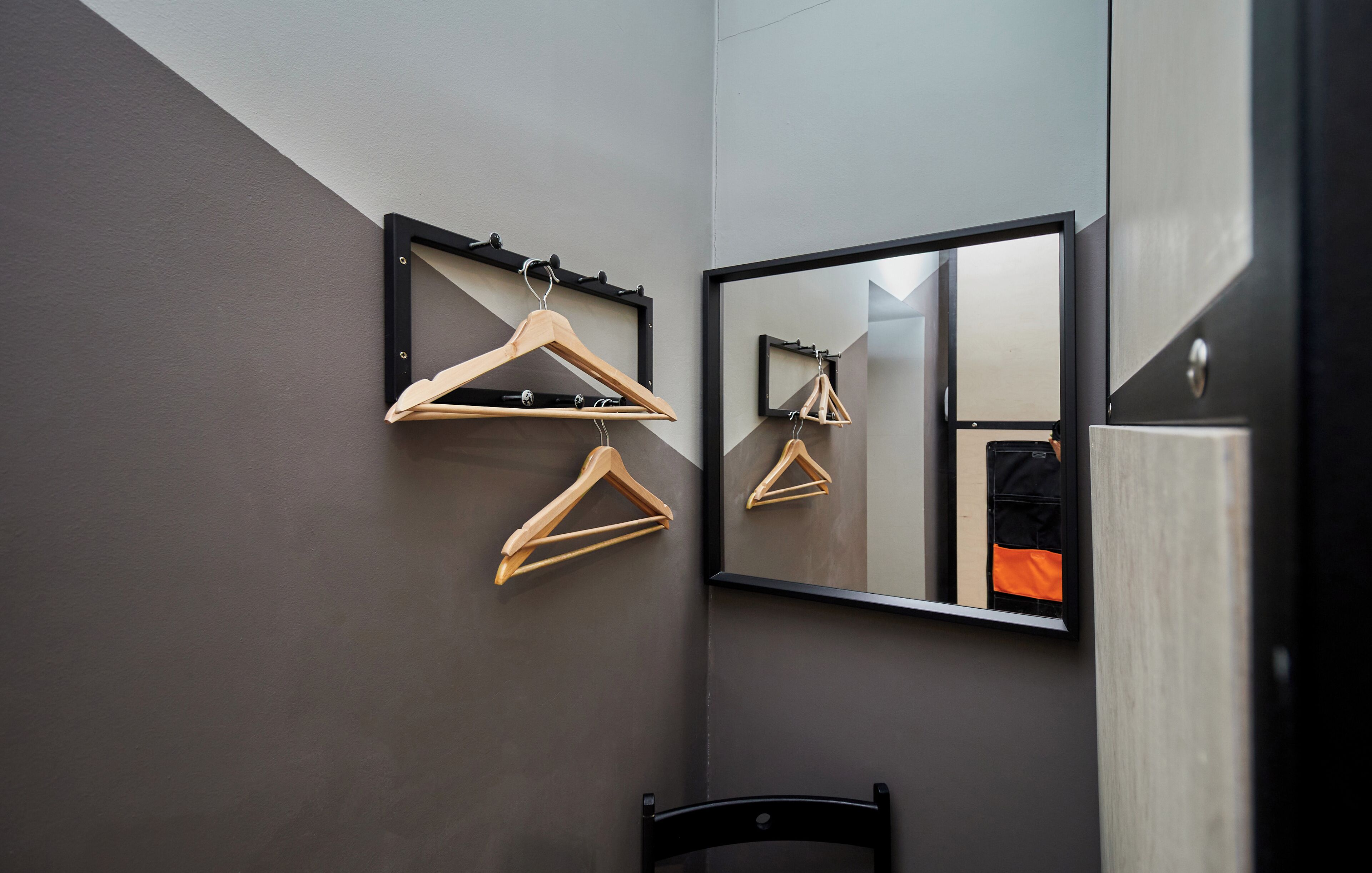A bathroom with a mirror, wooden hangers, and a black chair.