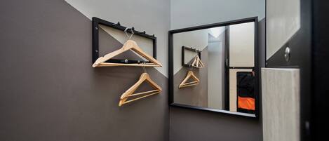 Une salle de bain avec un miroir, des cintres en bois et une chaise noire.
