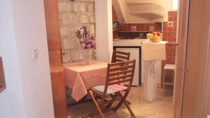 A narrow hallway leading to a dining area with a table and chairs, a stone wall, and a kitchen visible through an open door. - Apartments Abjanic - Studio with Terrace - Ilije Sarake 8 (Dubrovnik)
