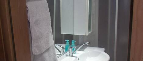 Une salle de bain avec un lavabo blanc, deux robinets, un miroir et une serviette suspendue à un porte-serviettes.