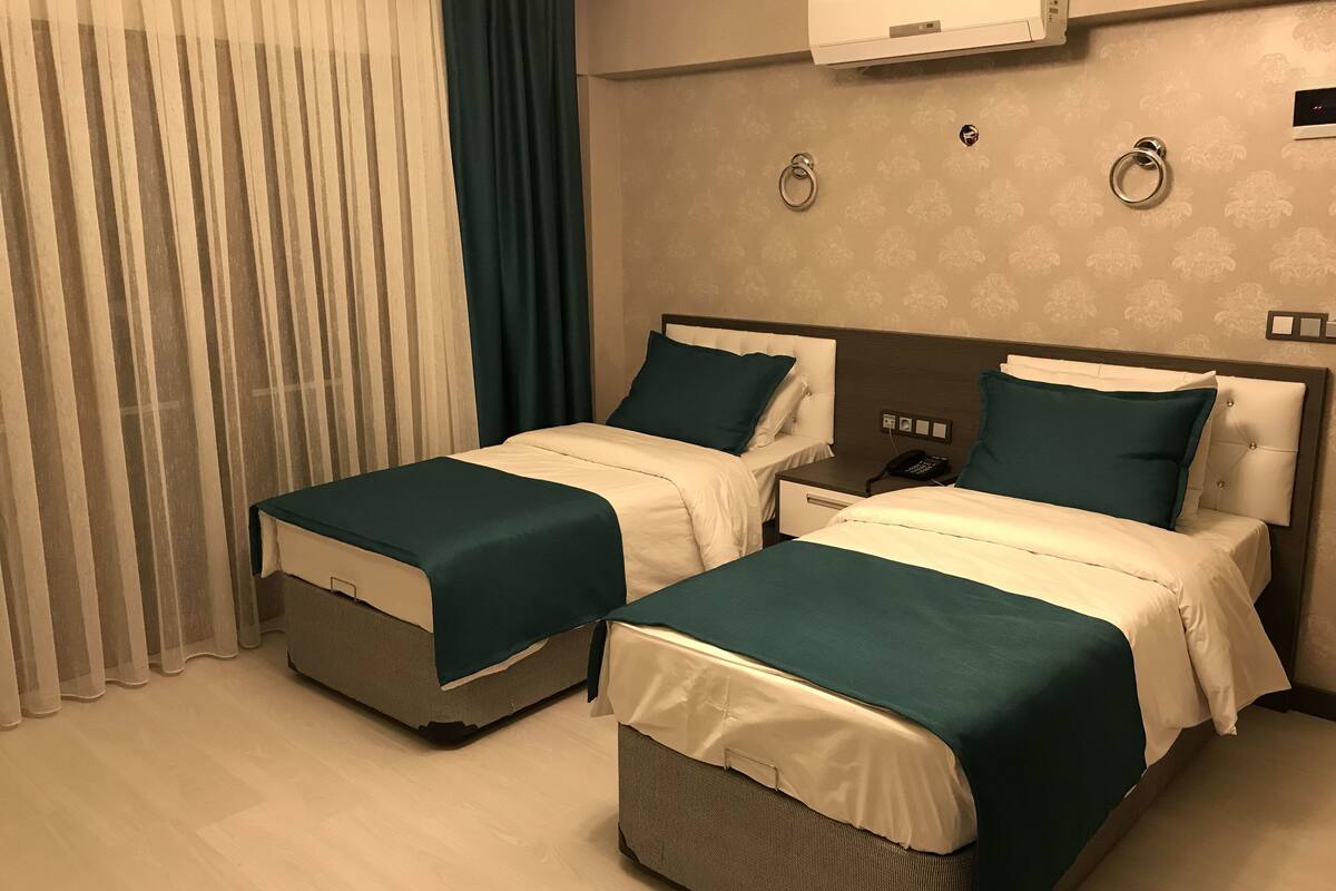 A hotel room with two beds, a bedside table with a phone, and an air conditioning unit on the wall.