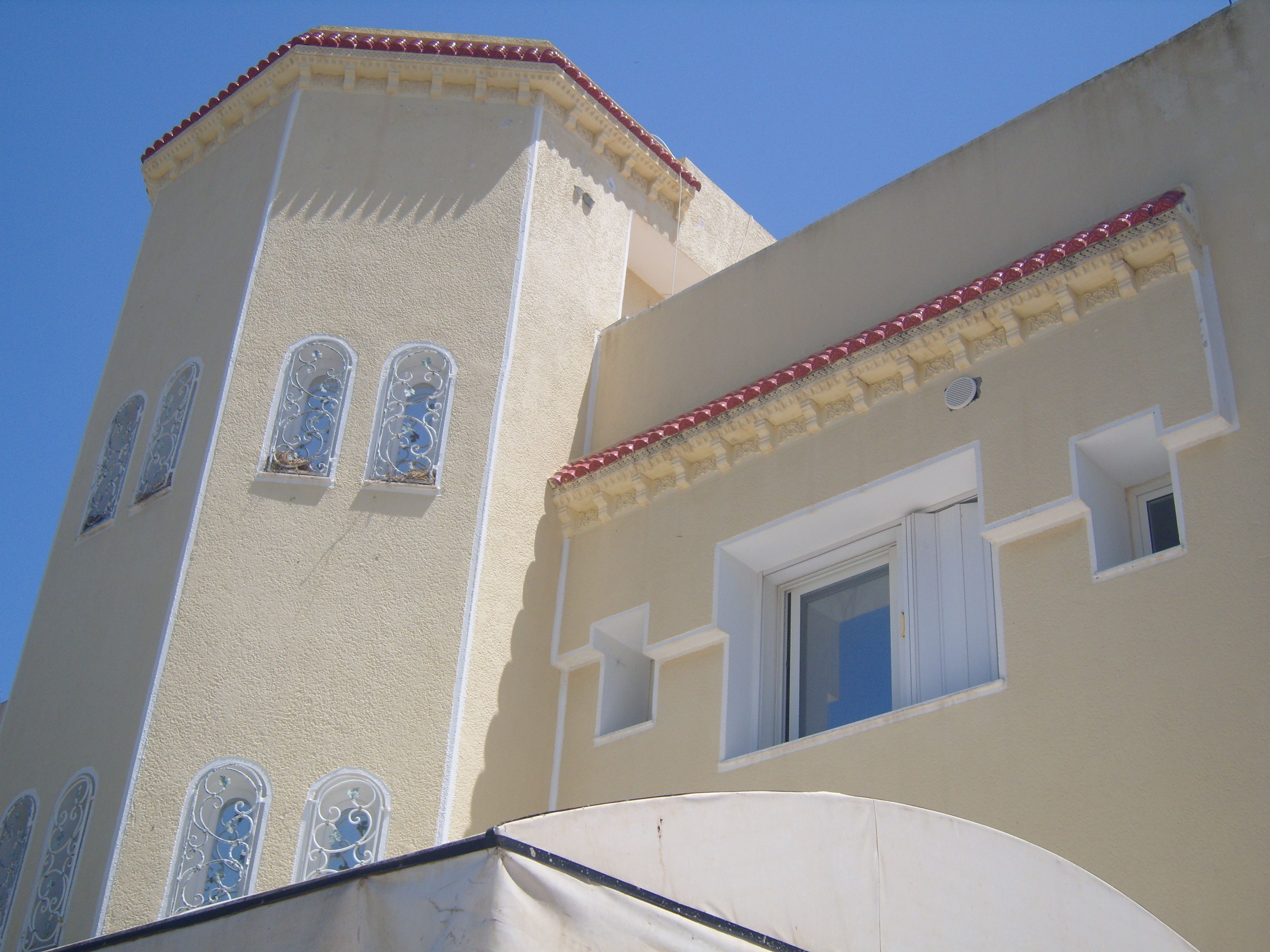 A building with a tower featuring arched windows and a flat roof with red trim.