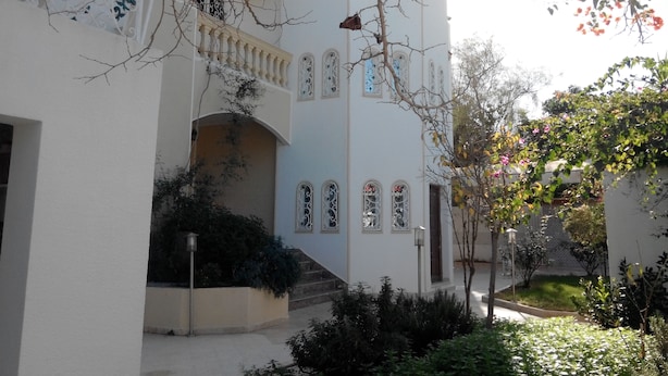 Un bâtiment à la façade blanche, doté de nombreuses fenêtres encadrées d’ornements décoratifs et d’un escalier menant à un étage supérieur.