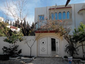 A courtyard with a white gate, a small tree, and a building with blue windows in the background.