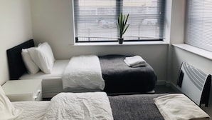 Ein modernes Hotelzimmer mit einem Bett, einer kleinen Sitzecke, einem Heizkörper und einem Fenster mit Jalousien.