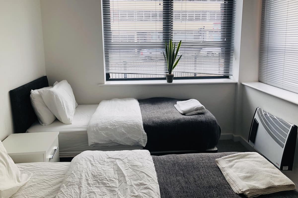 Habitación de hotel moderna con cama, un pequeño rincón de estar, un radiador y una ventana con persianas.