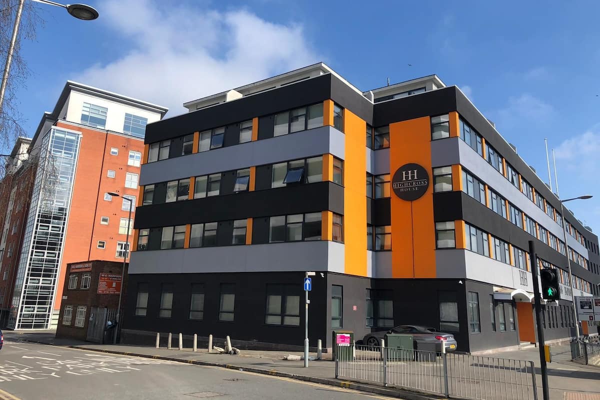 Un edificio moderno con un llamativo letrero 'HighCross House', que presenta una estructura de varios pisos con fachadas en tonos negros y naranja, ventanas amplias y una entrada visible a nivel de calle.