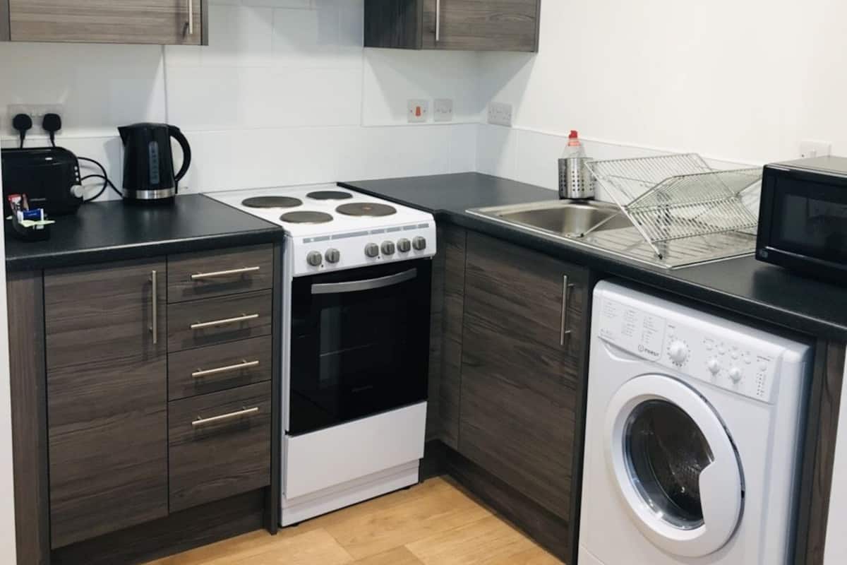 Una cocina compacta con armarios de madera oscura, una estufa blanca, horno empotrado, microondas y lavadora de carga frontal.