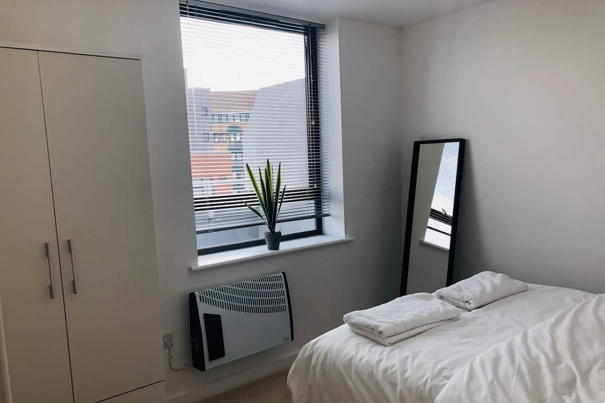 Un dormitorio con una cama, una ventana con persianas, un radiador y un armario.