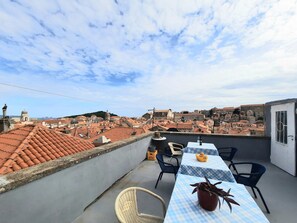 Een dakterras met een tafel en stoelen, een bloempot en uitzicht op een stadsbeeld met terracottadaken en historische gebouwen.
