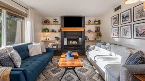 Un salon avec une cheminée, deux canapés, une table basse et des étagères ornées d’objets décoratifs.