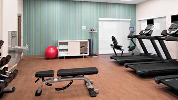 A gym with treadmills, a stationary bike, a bench, and a red exercise ball.