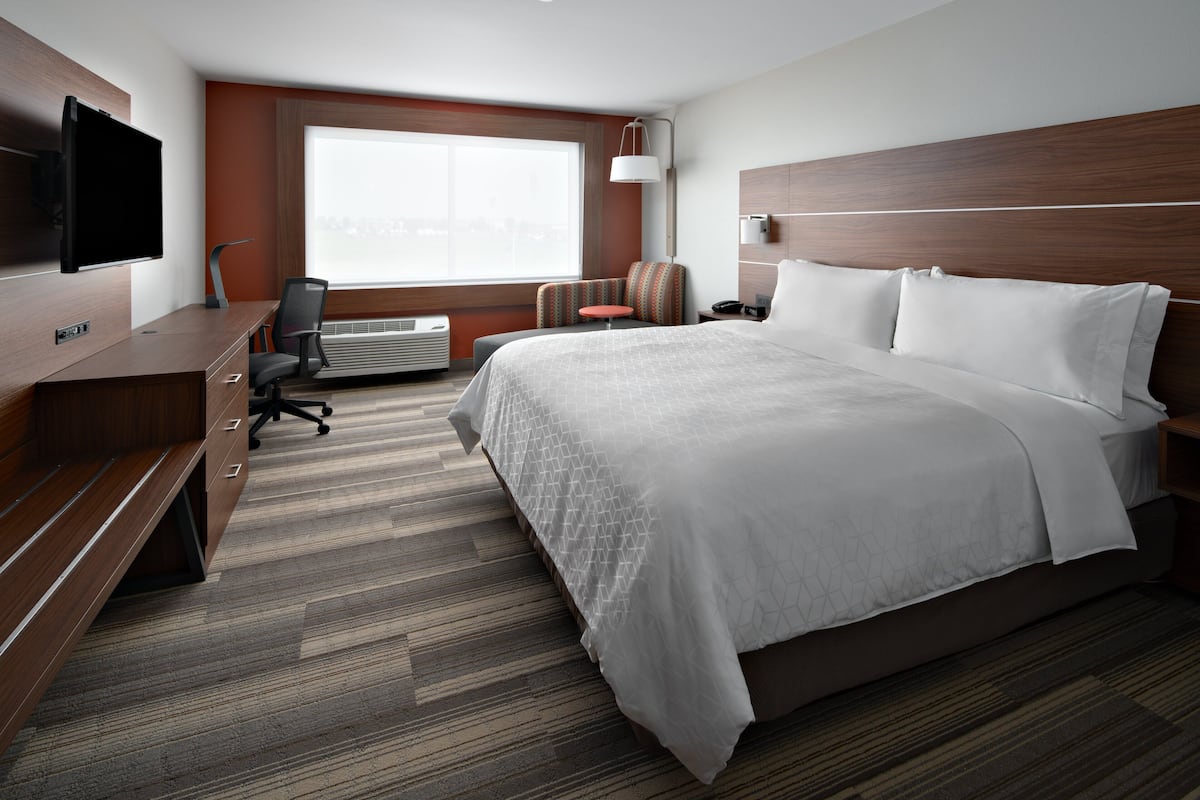 Ein Hotelzimmer mit einem großen Bett, einem Schreibtisch mit Flachbildfernseher, einem Sessel und einem Fenster mit Stadtblick.