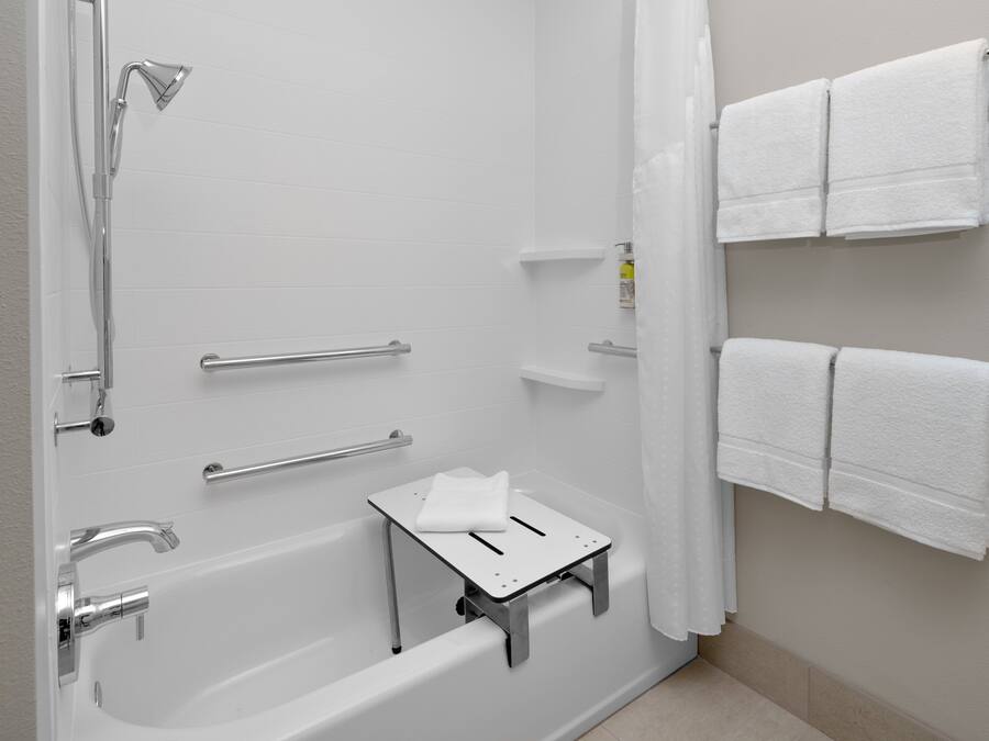 Ein modernes Badezimmer mit Badewanne, Dusche, Haltegriffen und weißen Handtüchern.