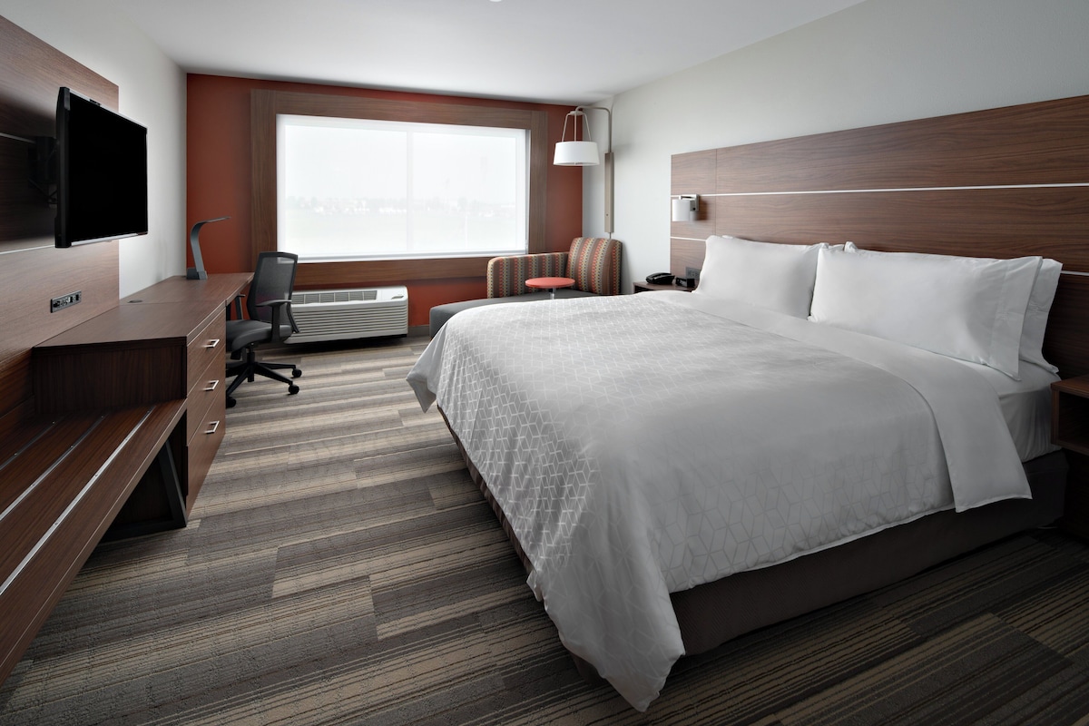 Quarto de hotel com cama, escrivaninha com televisão de tela plana, cadeira, mesinha e janela com vista para a cidade.