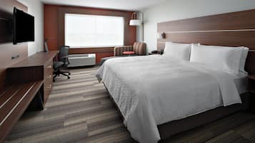 Habitación de hotel con cama, escritorio con televisor de pantalla plana, silla, mesita y ventana con vista a la ciudad.