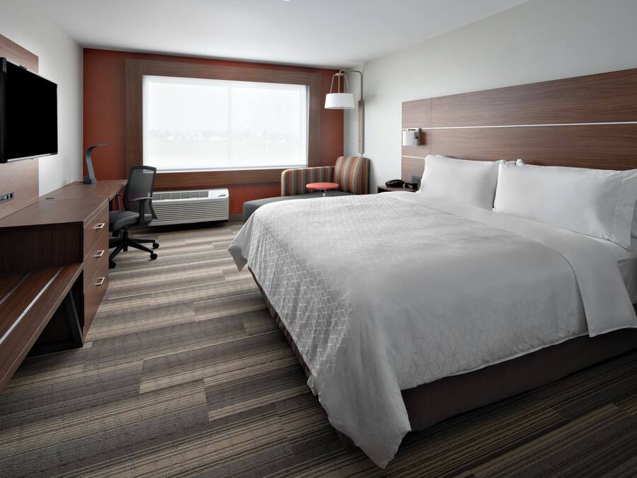 Habitación de hotel con cama, escritorio con televisor de pantalla plana, silla, mesita y ventana con vista a la ciudad.