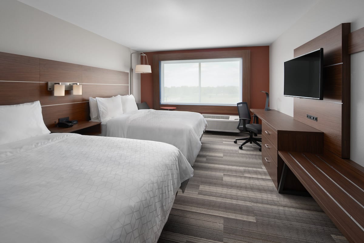 Ein Hotelzimmer mit zwei Betten, einem Fernseher, einem Schreibtisch und einem großen Fenster.