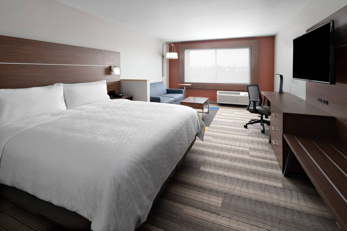 Ein Hotelzimmer mit einem großen Bett, einem Schreibtisch mit Stuhl, einem Fernseher und einem Fenster mit Blick.
