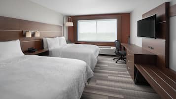 A hotel room with two beds, a desk, a TV, and a large window.