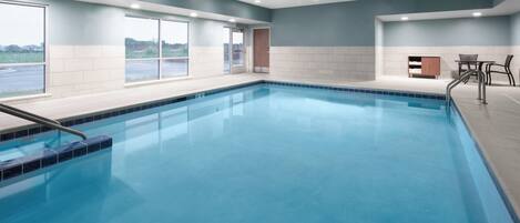 A swimming pool with clear blue water, surrounded by a tiled deck and a seating area with chairs.
