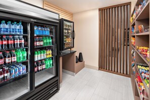 A beverage refrigerator stocked with various drinks, a snack shelf, and a wooden partition. - Holiday Inn Express & Suites Elkhorn - Lake Geneva Area by IHG (Elkhorn)