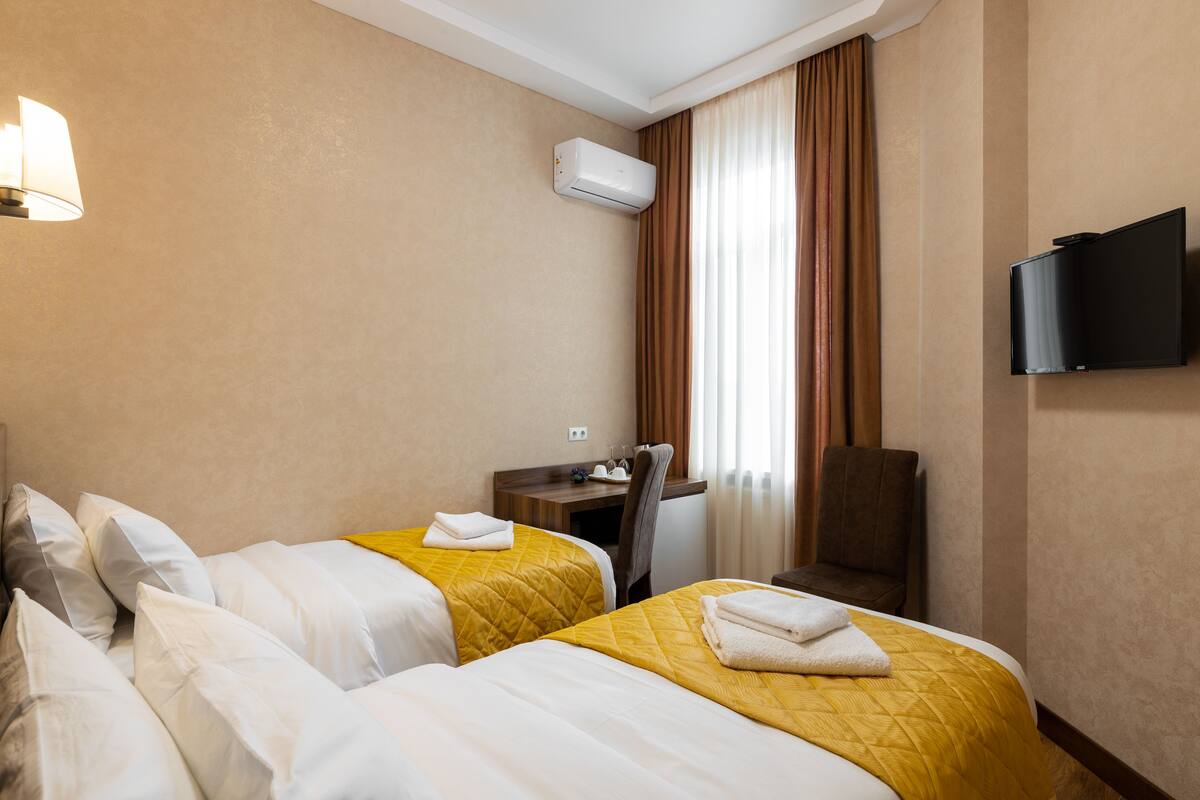 A hotel room with two beds, a desk, a chair, a TV, and an air conditioning unit.