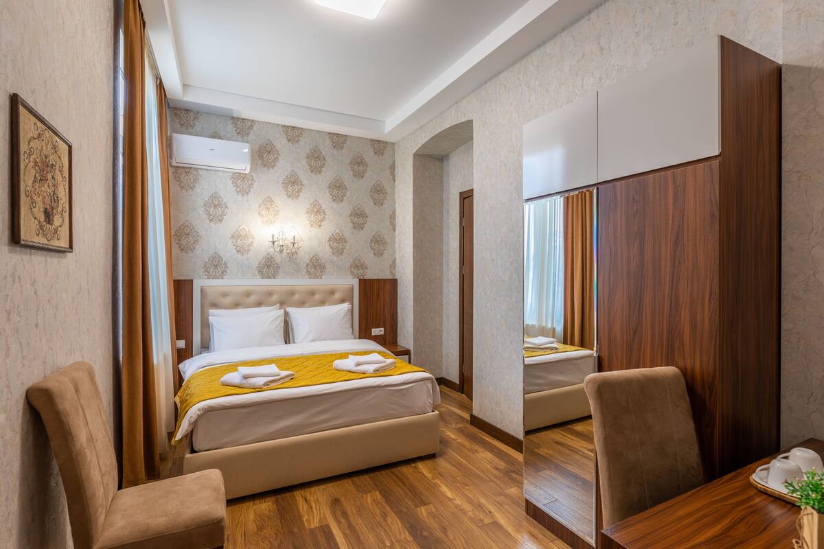 A hotel room with a bed, two chairs, a wooden table, and a mirror.